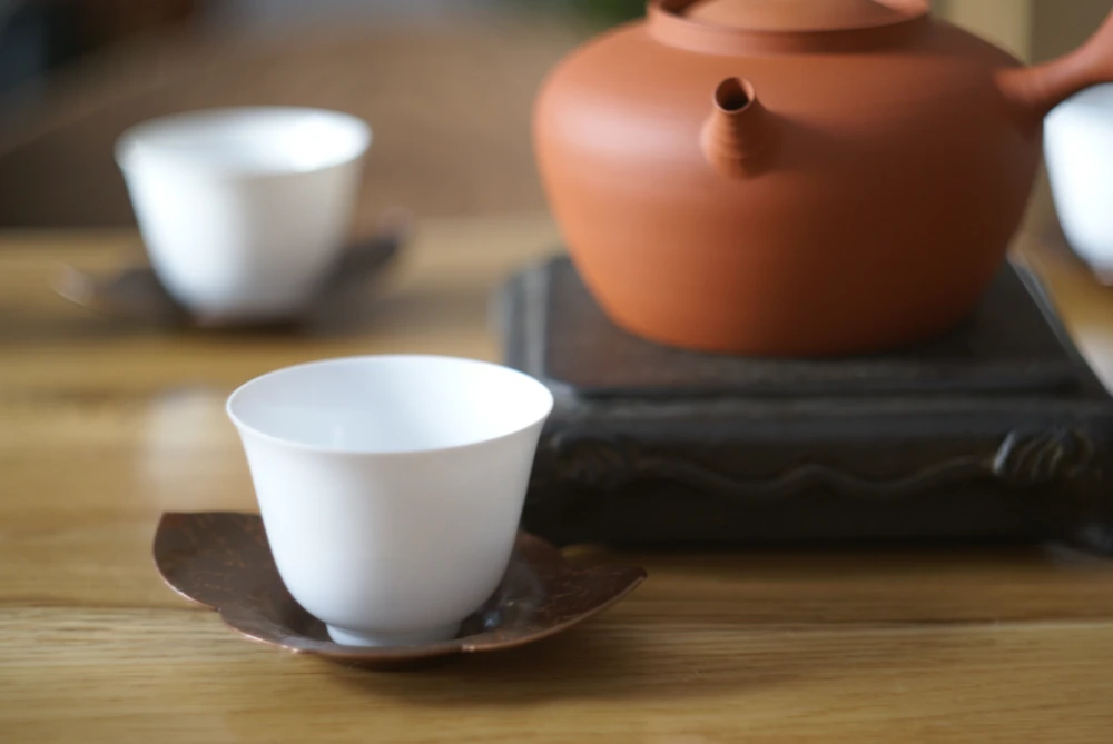 Фарфоровая чашка с чайником для воды на фоне